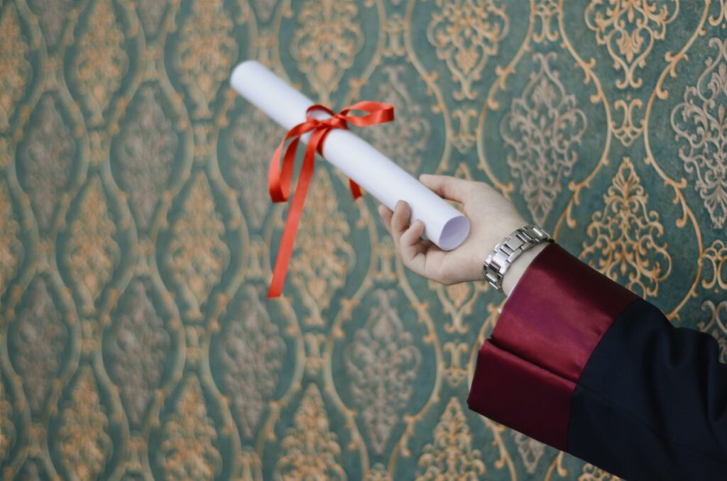 A graduate's hand holding a diploma with red ribbon, symbolizing achievement.
