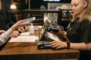Customer using mobile phone for contactless payment at a coffee shop counter with a barista.
