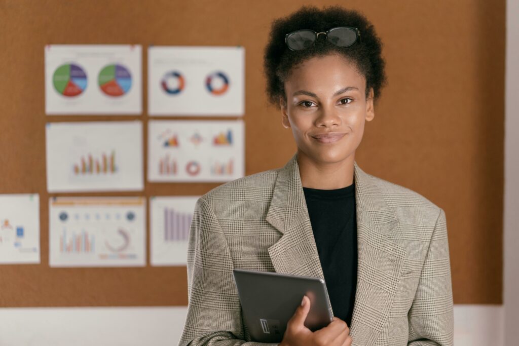 Confident woman in blazer with tablet standing in front of charts, conveying professional success.