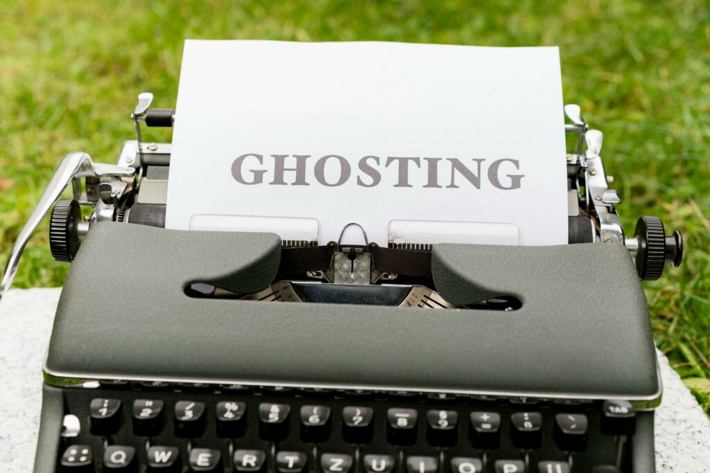 A vintage typewriter displaying the word 'Ghosting' on a white paper, set outdoors on grass.